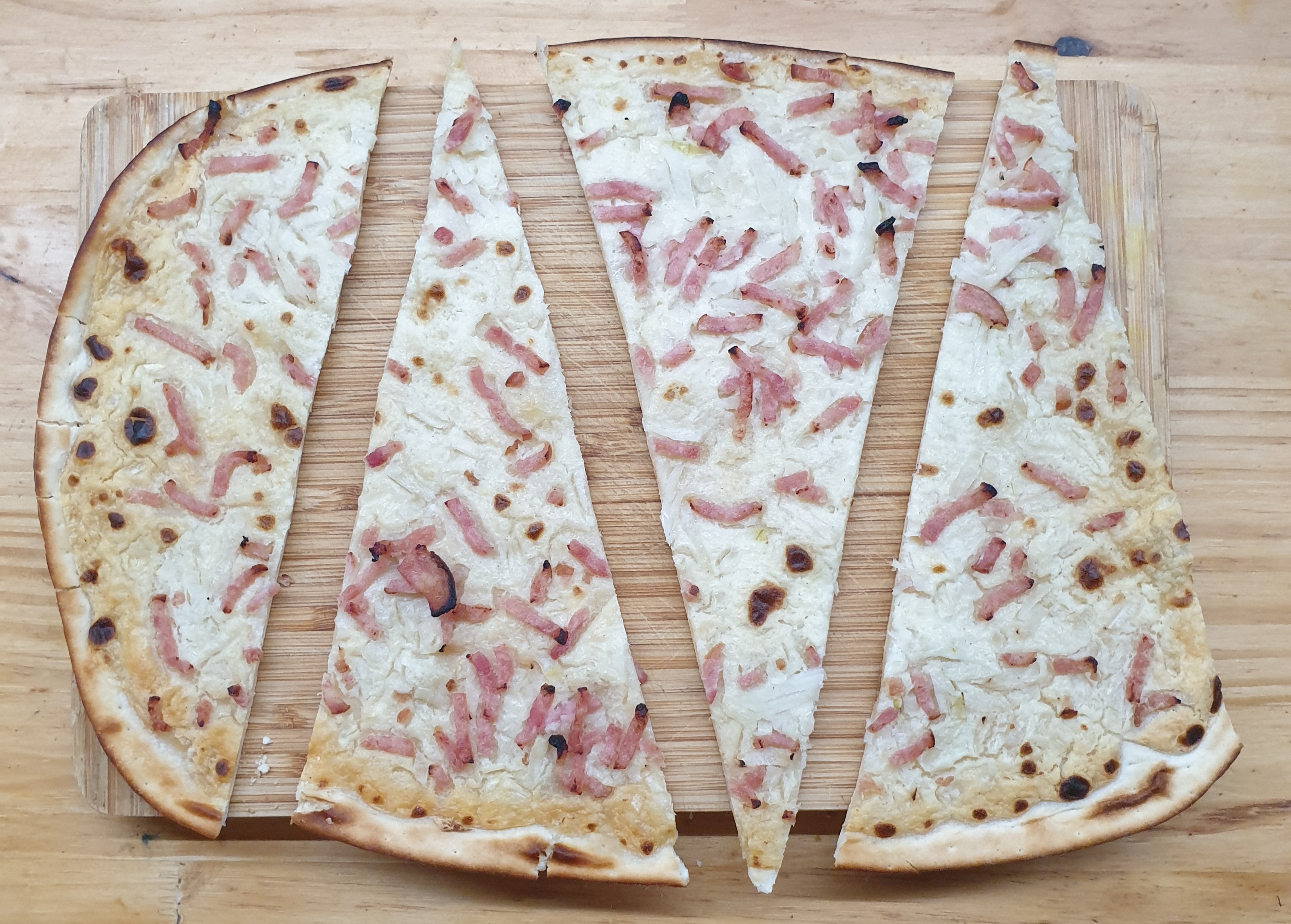 Tarte flambée, ook bekend als 'Flammkuchen', combineert een knisperende dunne bodem met romige crème fraîche, spek, en uien, voor een licht en hartig gerecht uit de Elzas.